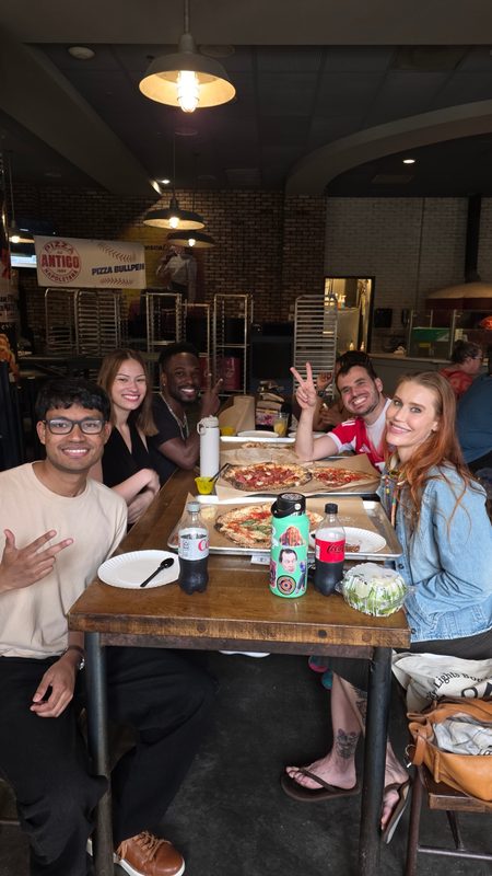 Five friends sitting around pizzas at a restaurant table