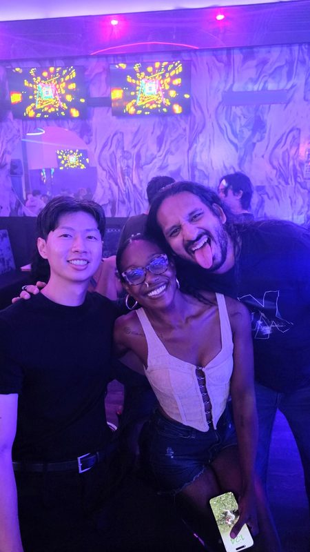 Three friends posing closely in a nightclub under purple and pink lights