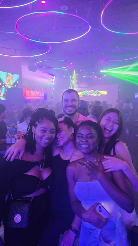 Four friends hugging and laughing under purple club lights