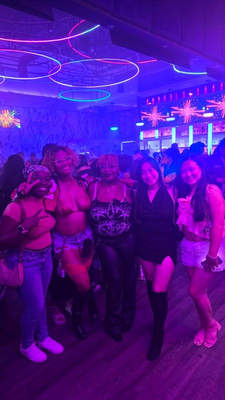 Five friends posing together in a nightclub under purple neon