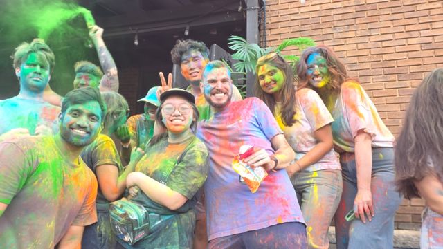 A big group smiling and covered in colorful Holi powder