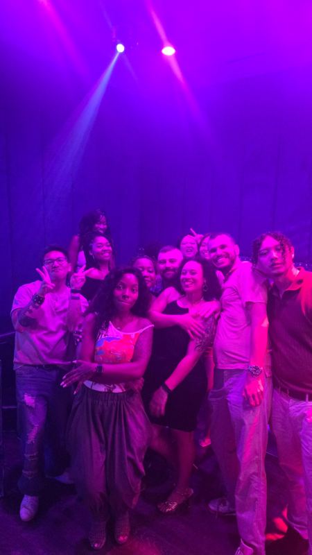 A group posing together under pink and purple stage lights